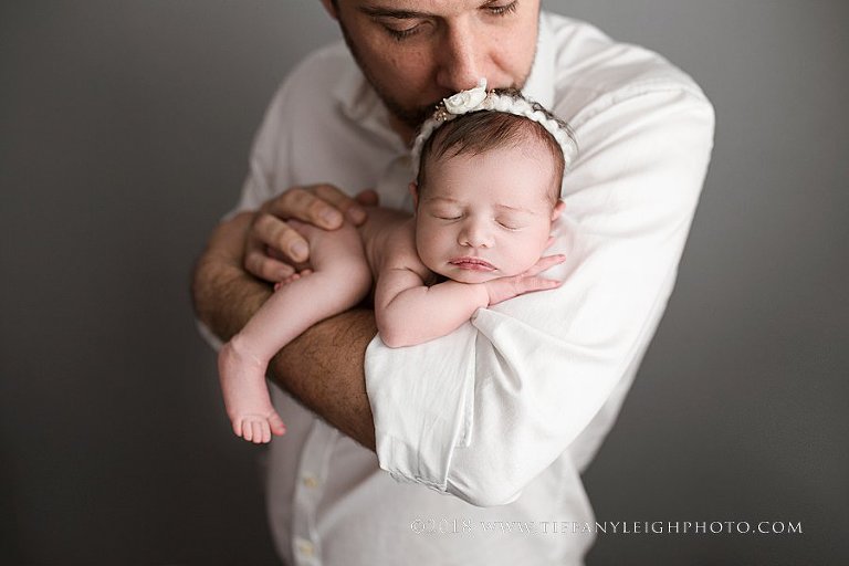 A newborn baby girl's leg hangs off of her daddy's arm while he holds her. 