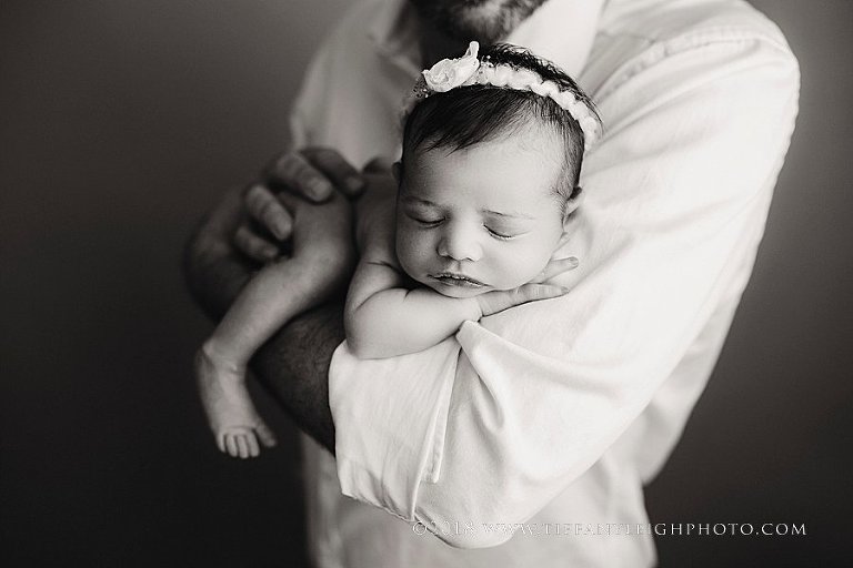 A baby girl sleeps on her dad's arm. 