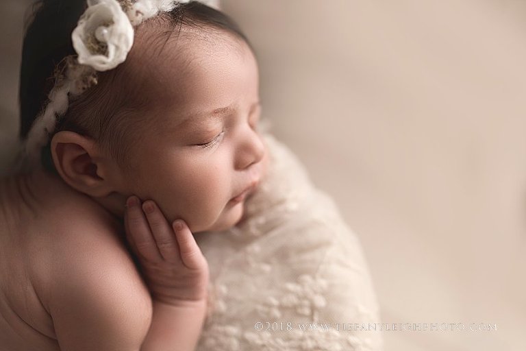 A newborn baby sleeps with her hand up hear her face. 