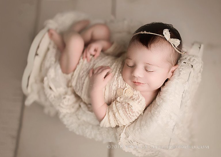 A newborn baby wears a lace onesie. 