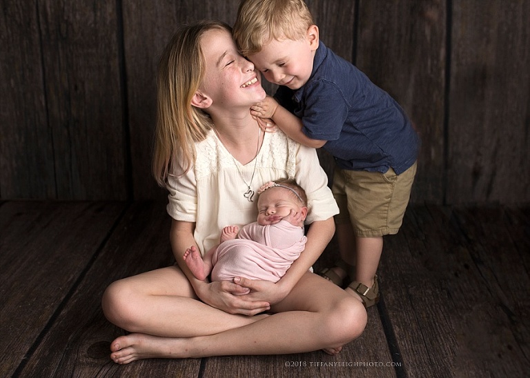 A little girl holds her new sister and laughs with her little brother