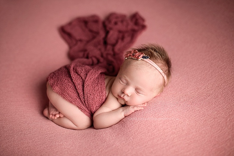 A newborn baby sleeps with a rose colored blanket on top of her