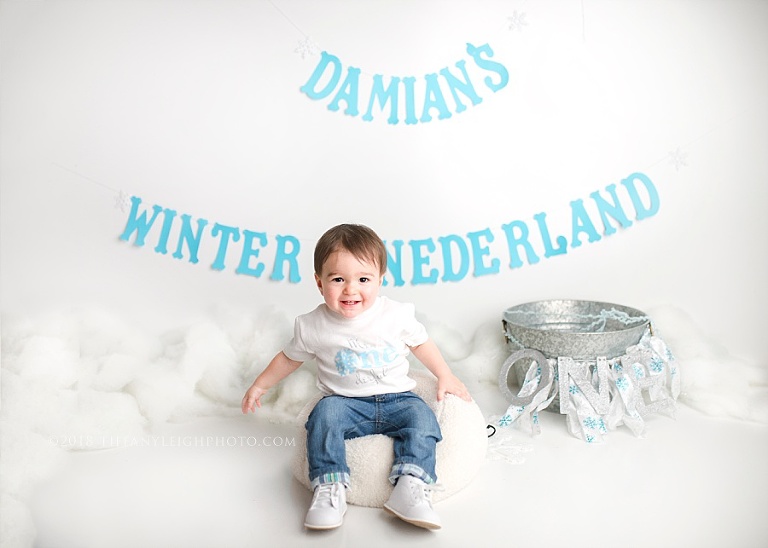 A baby boy sits in front of some birthday decorations. 